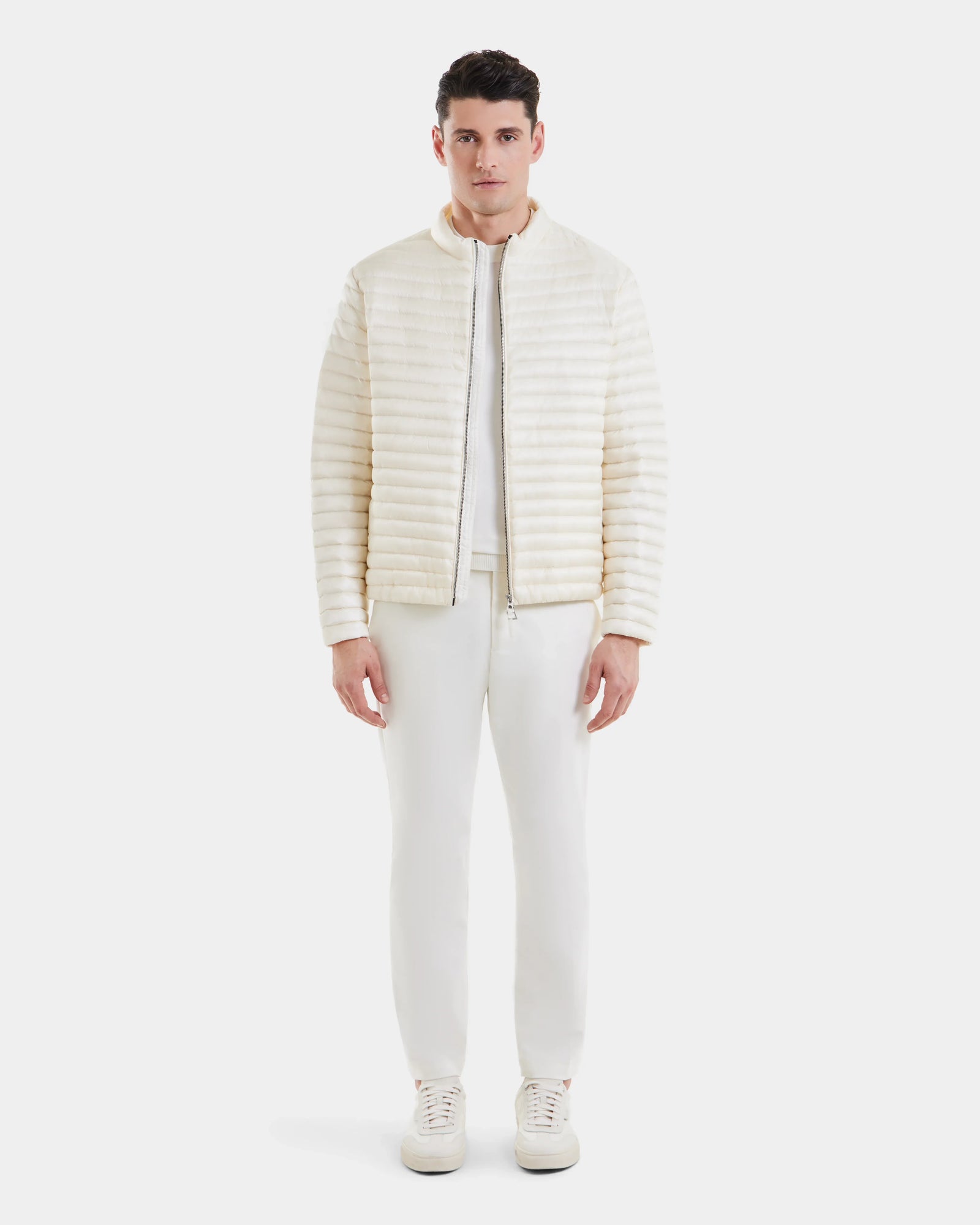 A man faces forward wearing Rudsaks REYMOND - M125013 Iceland mens down jacket, made from RDS-certified down and recycled nylon, paired with white pants and sneakers, set against a plain white background.