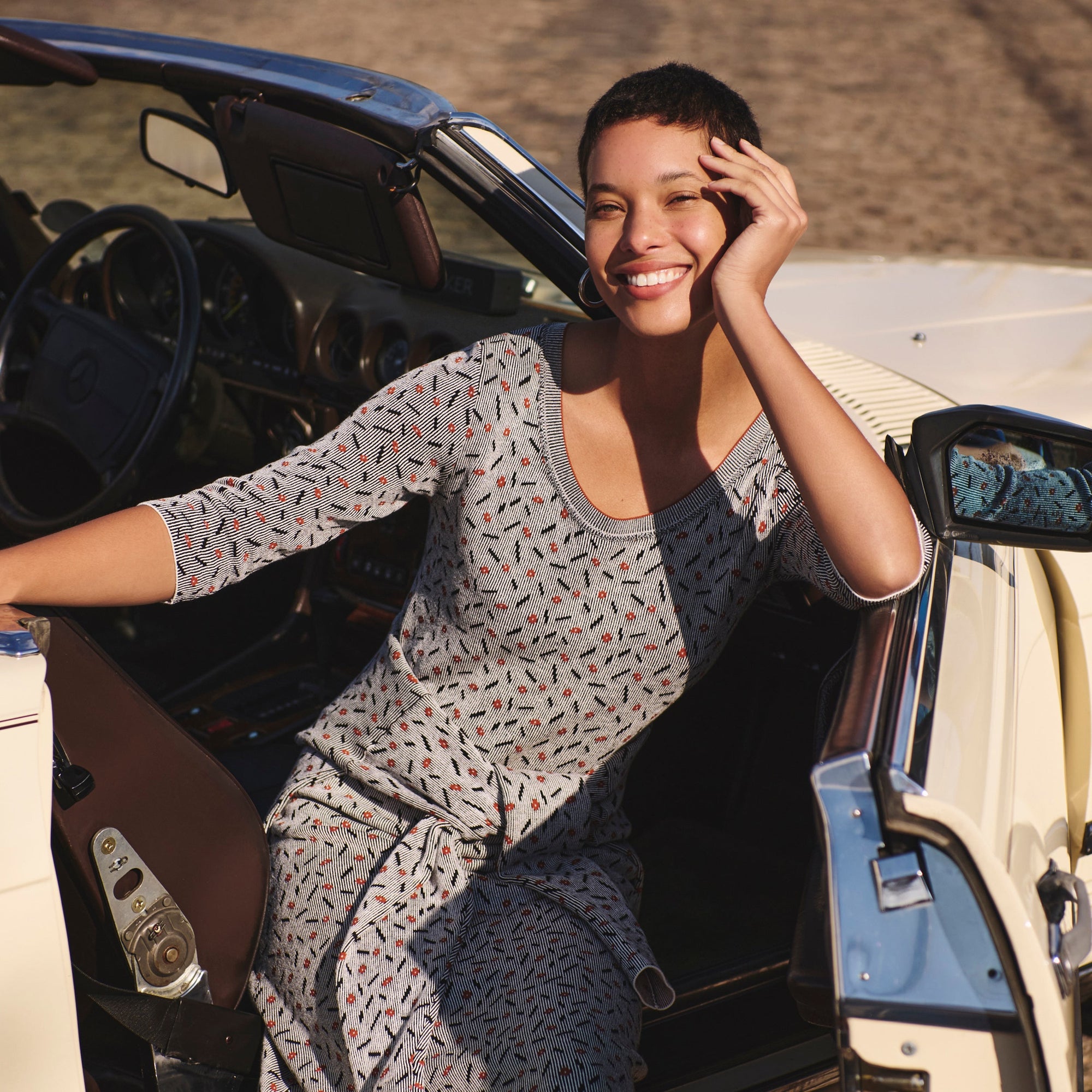 Front image of a woman sitting in a car wearing the Tippy Dress in Brick and Black