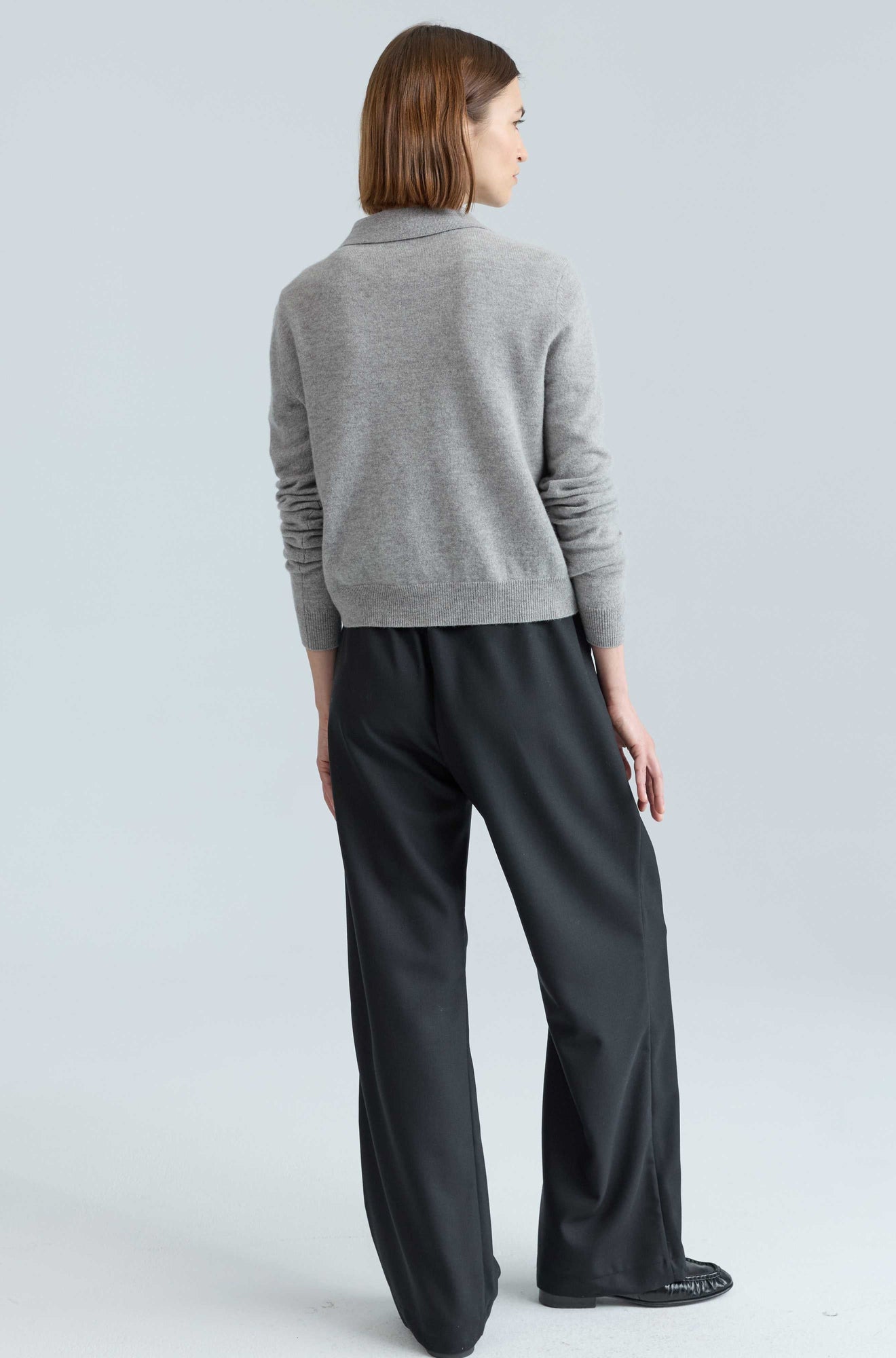 Woman wearing a gray sweater and black pants on a light gray background
