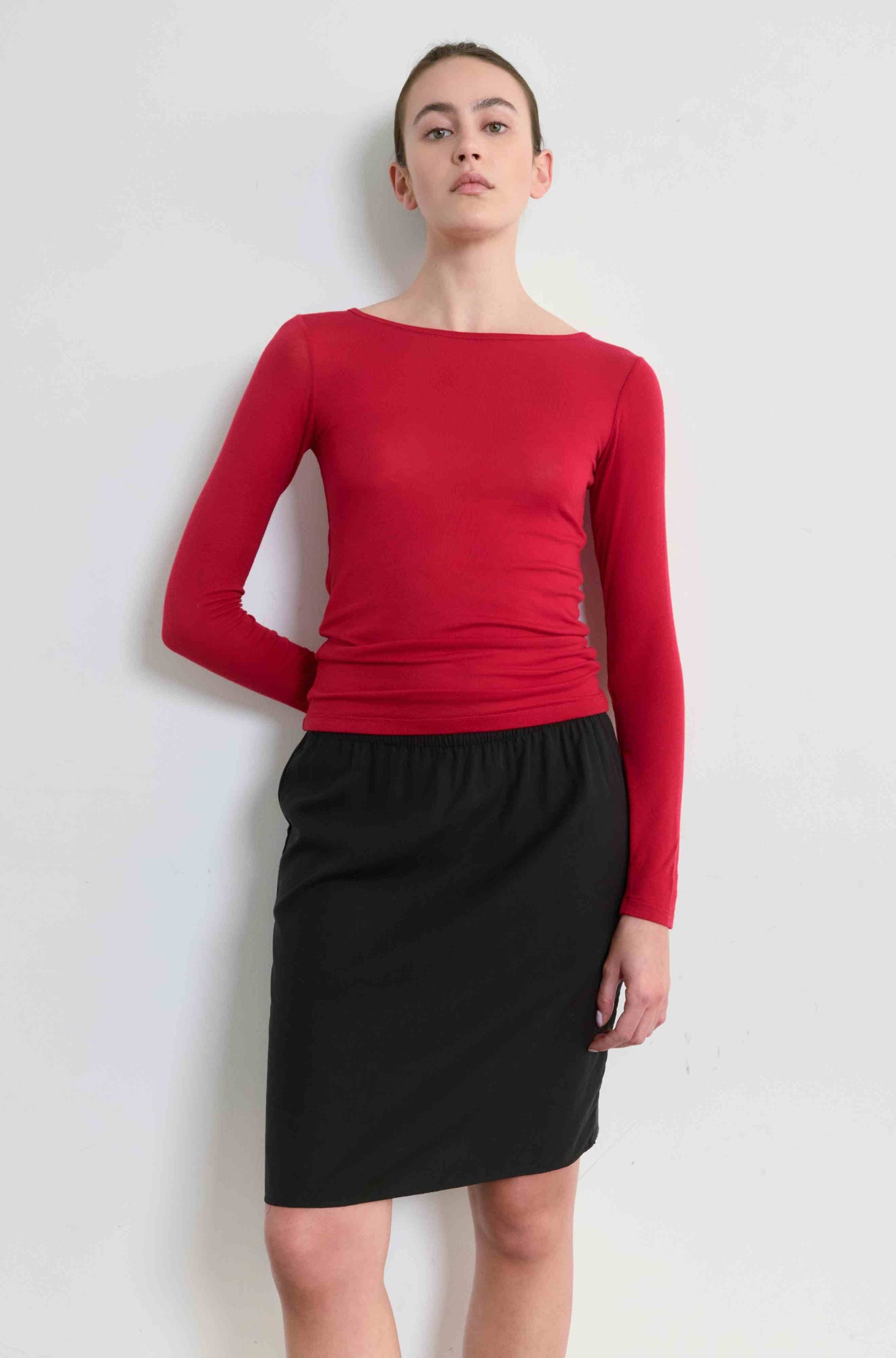 Person wearing a red long-sleeve top and black skirt on a white background