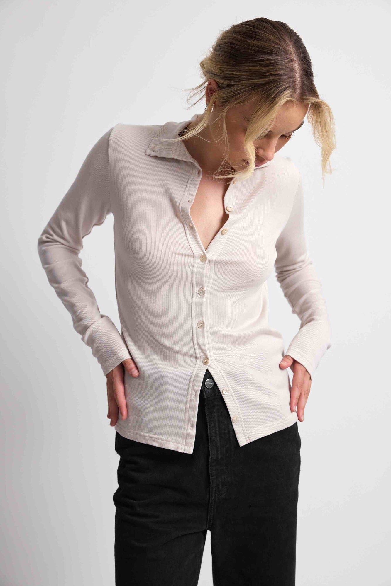 Woman wearing a pink button up top with black bottoms on a light grey background