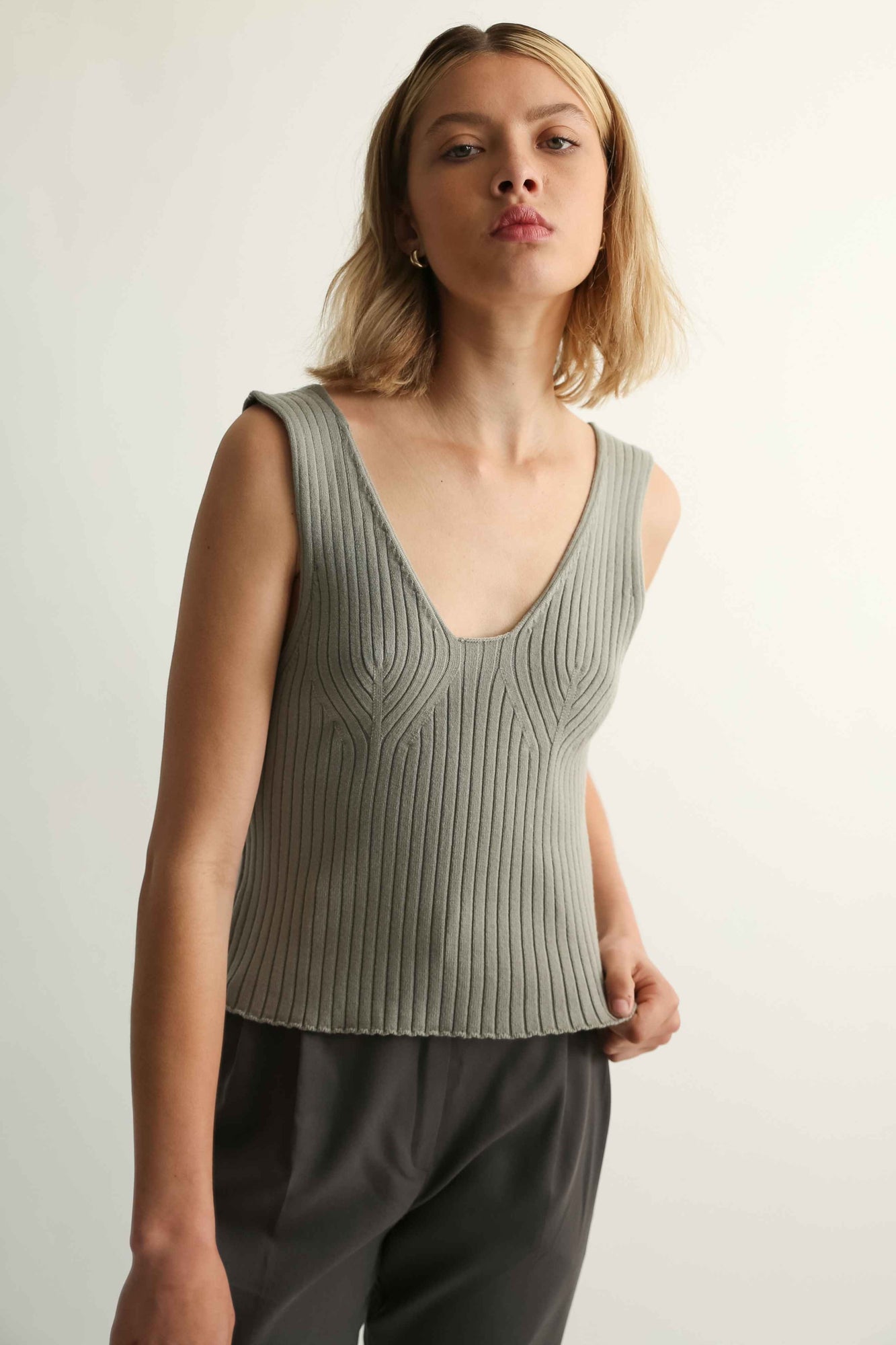Woman wearing a sleeveless ribbed top and dark pants against a plain background