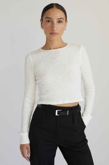 Woman wearing a white long-sleeve top and black pants against a plain background