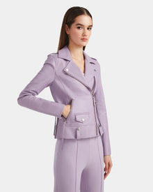 A woman with straight brown hair wears the Rudsak MERGO - 8124034 Lilac Foam biker jacket and matching pants, standing with one hand in her jacket pocket against a plain white background.