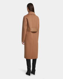 A woman faces away, wearing the Rudsak LAYLAH - 8124699 Camel knee-length wool coat with a wide back belt and black knee-high boots. Her straight hair is down, set against a plain white background.