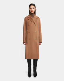 A woman faces forward in the Rudsak LAYLAH - 8124699 Camel womens wool coat—knee-length, double-breasted—over a brown turtleneck and black knee-high boots, set against a plain white background.