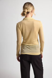 Person wearing a beige long-sleeve top and black pants on a white background