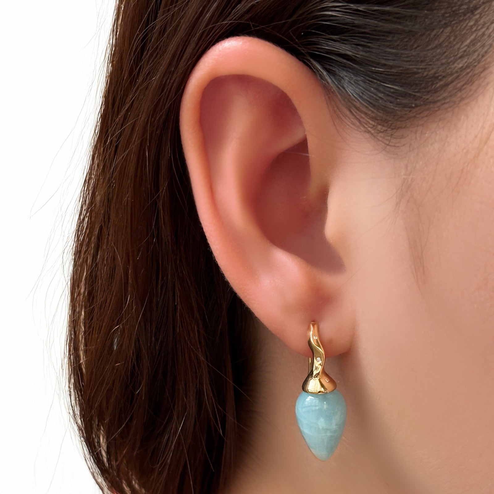 Aquamarine drop earrings with yellow gold and diamond ripple bales, on a model's ear.
