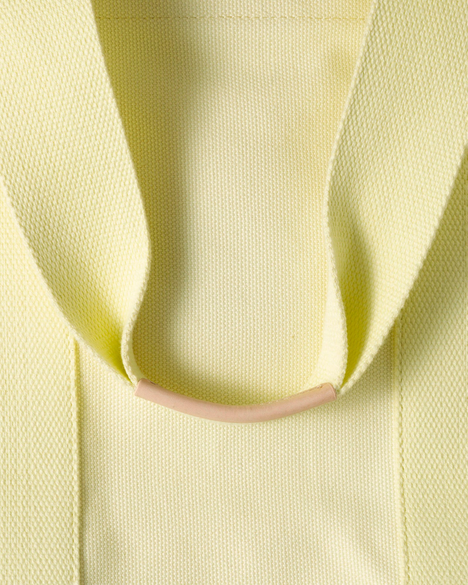 Close-up of a textured pale yellow fabric folded with a beige horizontal ring at the center by graf lantz. Its knit creates a symmetrical, minimalist design, perfect for radiating laid-back elegance on beach days.