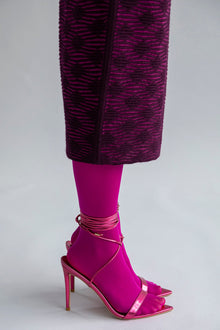Detail shot of the textured pattern on the fuchsia aubergine Ines skirt, styled with bright pink sheer tights and laced-up high heels.