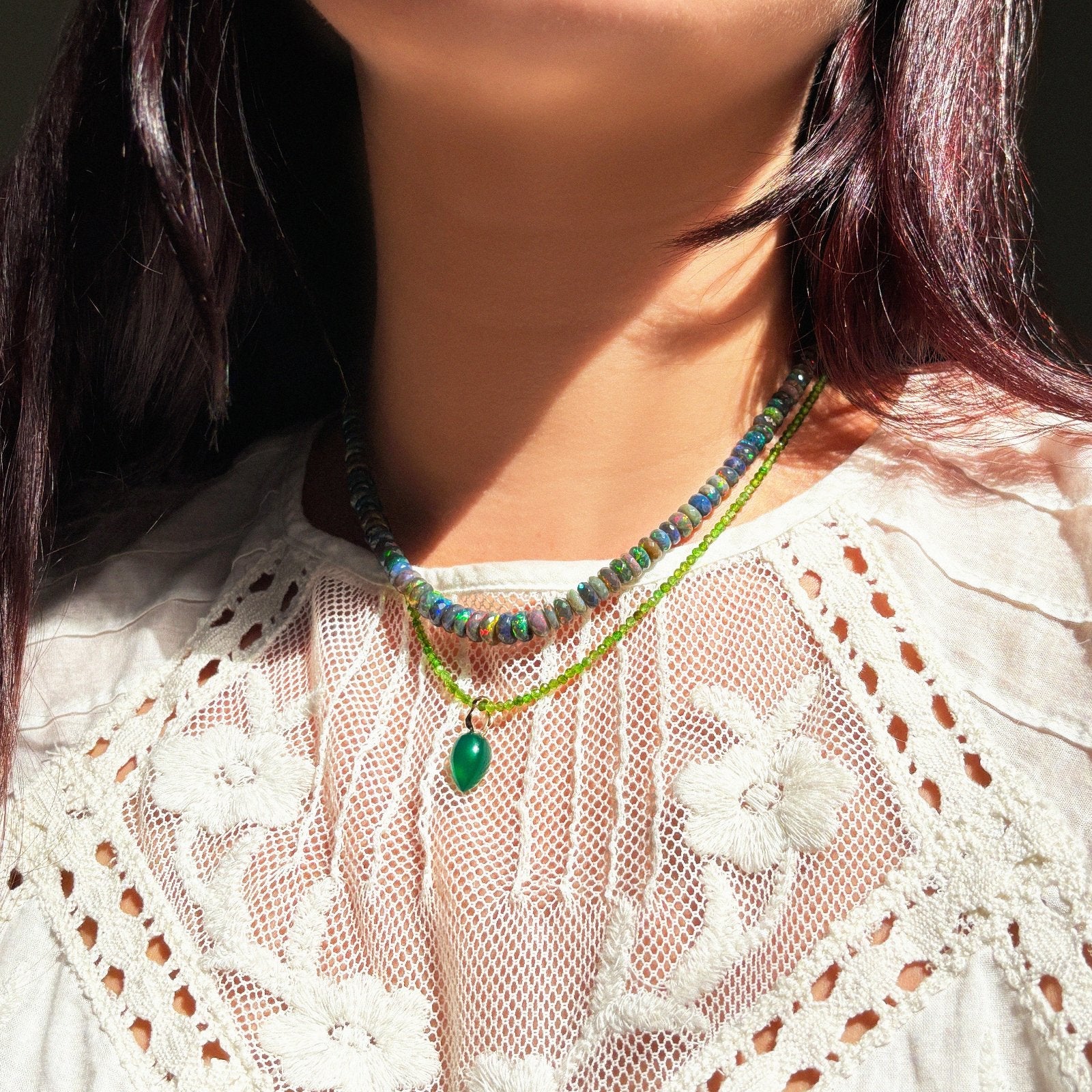 Shimmering beaded necklace made of faceted opals in shades of green, yellow, and blue on a gold linking ovals clasp, layered with a gemstone necklace and acorn, on a neck.