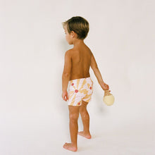Child wearing white swim trunk with red and yellow sun print design, shown from side angle.