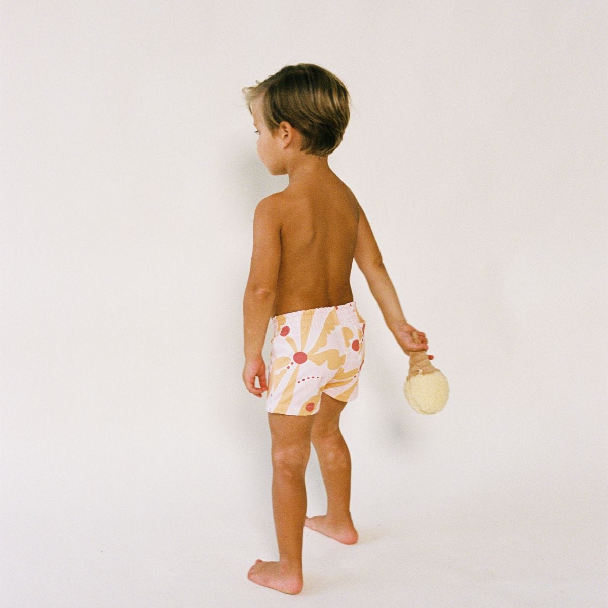 Child wearing white swim trunk with red and yellow sun print design, shown from side angle.