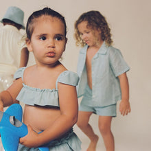 Toddler wearing powder blue short-sleeve button-down shirt with ruffled neckline and matching shorts.