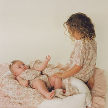 Two children wearing cream button-down shirts with small floral print in rust and green tones.