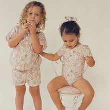 Two toddlers wearing matching cream and rose floral button-down shirts with short sleeves.